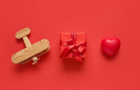 Wooden airplane with gift and heart on red background. Valentine's Day celebrationの写真素材