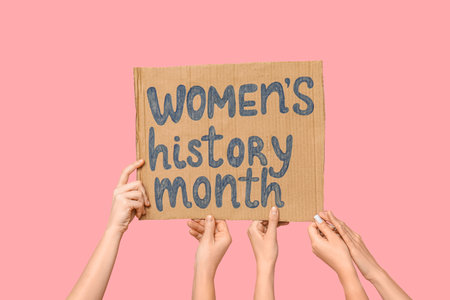 Female hands holding cardboard with text WOMEN'S HISTORY MONTH on pink backgroundの写真素材