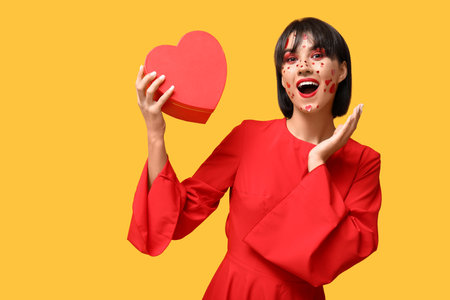 Beautiful young woman with creative makeup and gift for Valentines Day on yellow backgroundの写真素材