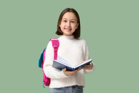 Little schoolgirl reading book on green background