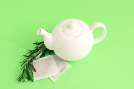 Teapot of hot rosemary tea on green background