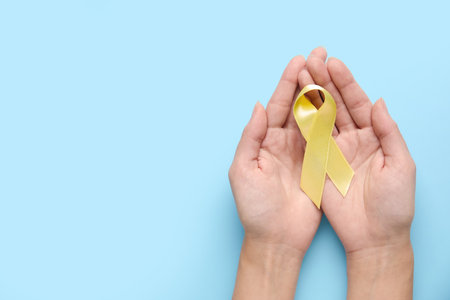 Female hands with golden awareness ribbon on blue background. International Childhood Cancer Dayの写真素材