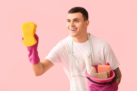 Young man with cleaning supplies on pink background