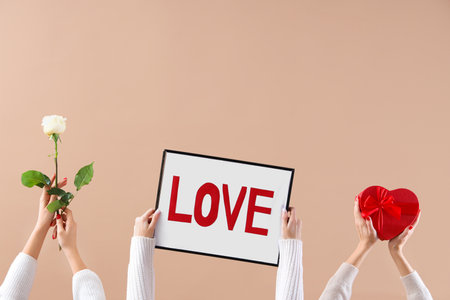 Female hands holding frame with the word LOVE, heart and beautiful rose on beige background. Valentine's Day celebrationの写真素材