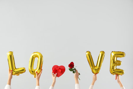 Female hands holding heart-shaped gift box, rose and word LOVE made from balloons on white background. Valentine's Day celebrationの写真素材