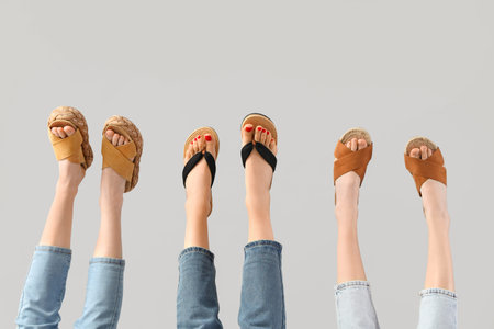 Female legs wearing different sandals on gray background