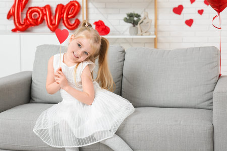 Cute little girl with paper heart sitting in room decorated for Valentines Dayの写真素材