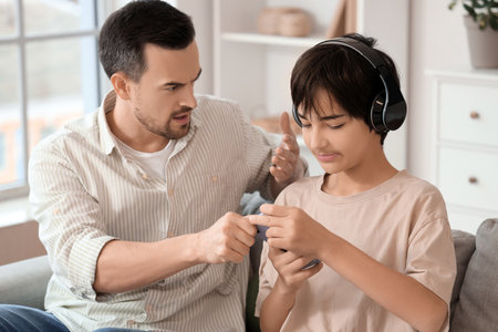 Angry father taking mobile phone away from his teenage son at home. Family problem conceptの写真素材