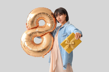 Beautiful young woman with balloon in shape of figure 8 and gift on gray background. International...