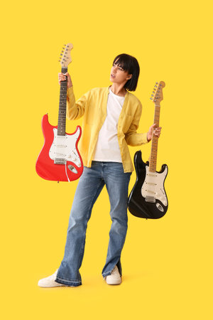 Cool young woman with electric guitars on yellow backgroundの写真素材