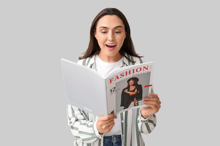 Young woman reading fashion magazine on light backgroundの写真素材