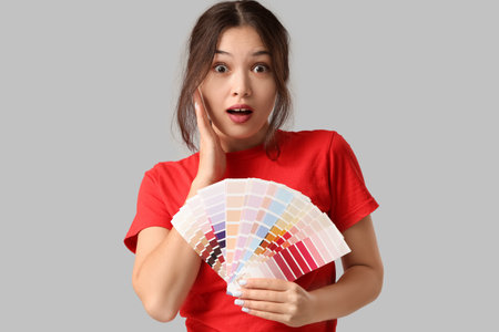 Surprised young woman with different palette samples on gray backgroundの写真素材