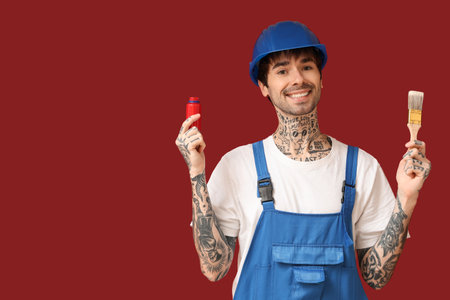 Happy male painter holding bottle of paint and brush on color backgroundの写真素材