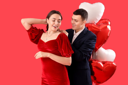 Young man putting necklace on his girlfriend against red background. Valentine's Day celebrationの写真素材