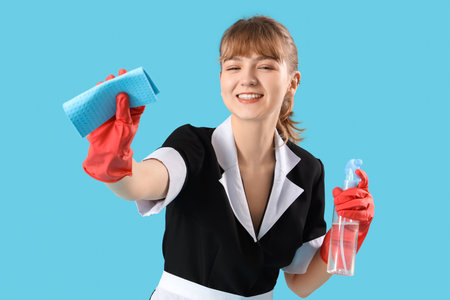Young chambermaid with rag and detergent on blue backgroundの写真素材
