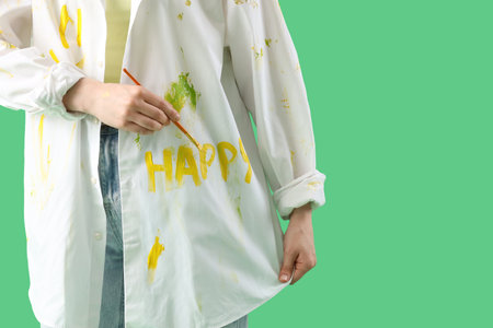 Female artist with paint brush and word HAPPY on her shirt against green background, closeupの写真素材