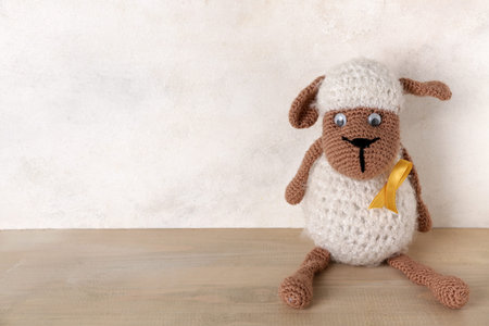 Toy sheep with golden ribbon on light wooden table against white grunge background. Childhood cancer...