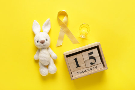 Toy bunny with golden ribbon, calendar and pacifier on yellow background. Childhood cancer awareness conceptの写真素材