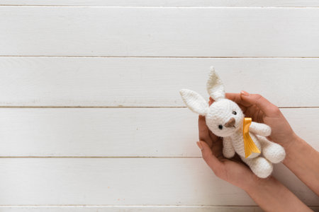 Hands with toy bunny and golden ribbon on white wooden background. Childhood cancer awareness conceptの写真素材