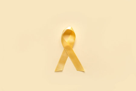 Golden ribbon on yellow background. Childhood cancer awareness concept
