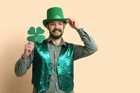 Young man in leprechaun hat with green beard holding clover on beige background. St. Patrick's Day celebrationの写真素材