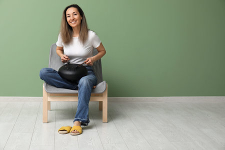Beautiful mature woman with sticks playing glucophone and sitting on chair near green wall