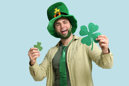 Young man in leprechaun hat with green beard holding clover on blue background. St. Patrick's Day celebrationの写真素材