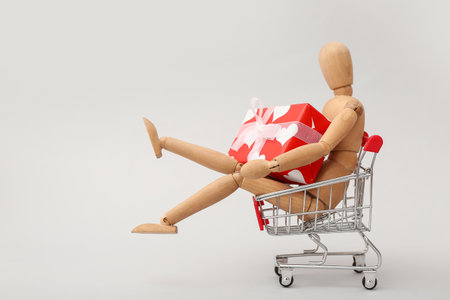 Small shopping cart with wooden human figurine and gift box on white background. Valentine's Day celebrationの写真素材