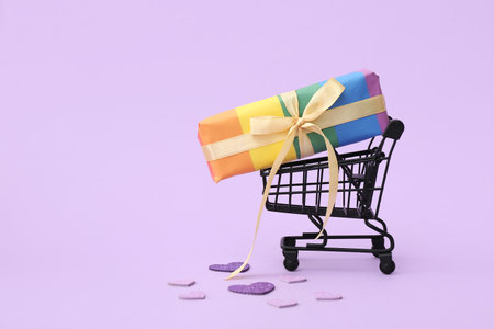 Small shopping cart with rainbow LGBT gift box on lilac background. Valentine's Day celebrationの写真素材