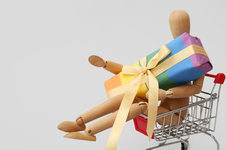 Small shopping cart with wooden human figurine and rainbow LGBT gift box on white background. Valentine's Day celebrationの写真素材