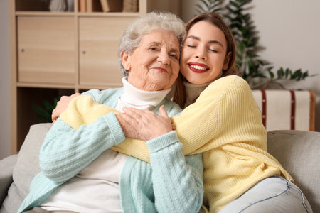 Young woman hugging her grandmother on sofa at homeの写真素材