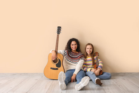 Young woman and girl with acoustic guitars sitting on beige backgroundの写真素材