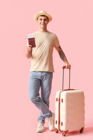 Young male tourist with suitcase and passport on pink backgroundの写真素材