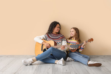Young woman and girl playing acoustic guitars together on beige backgroundの写真素材
