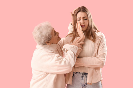 Senior woman hugging her crying granddaughter on pink backgroundの写真素材