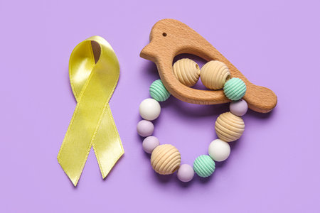 Golden ribbon with rattle on lilac background. Childhood cancer awareness conceptの写真素材
