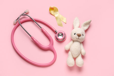 Golden ribbon with toy bunny and stethoscope on pink background. Childhood cancer awareness conceptの写真素材