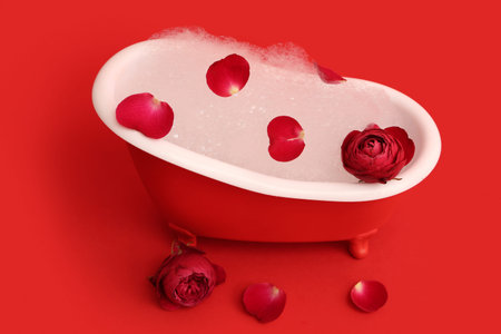 Mini bathtub with soap foam, roses and petals on red background. Valentine's Day celebration