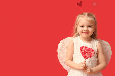 Cute little girl dressed as cupid with heart-shaped lollipop on red background. Valentine's Day...