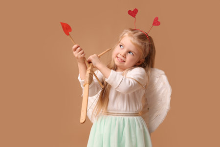 Cute little thoughtful girl dressed as cupid with bow and arrow on brown background. Valentine's Day celebrationの写真素材