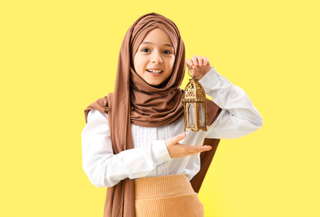 Little girl in hijab holding Muslim lantern on yellow backgroundの写真素材