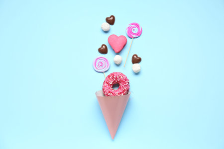Party cone with different tasty sweets on blue background. Valentine's Day celebration