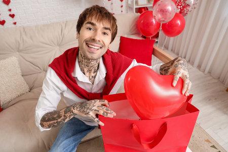 Handsome young man with shopping bag and heart-shaped air balloon at home. Valentine's day celebrationの写真素材