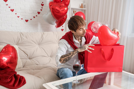 Handsome young man with shopping bag and heart-shaped air balloon at home. Valentine's day celebrationの写真素材