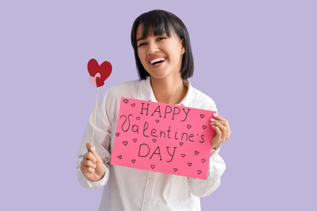 Beautiful young woman with paper hearts and gift card on lilac background. Valentine's day celebrationの写真素材