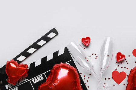 Movie clapper with heart shaped air balloons, champagne glasses and candles on gray background. Valentine's Day celebrationの写真素材