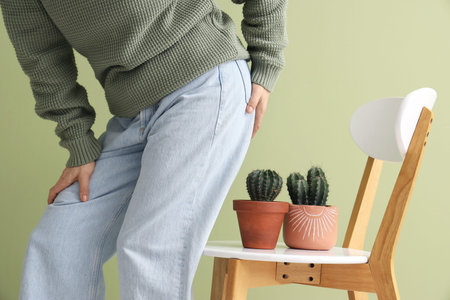 Mature woman with hemorrhoids and cacti on chair against green background, closeup