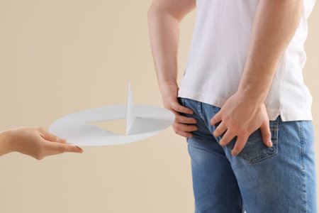 Hand with paper thumbtack and young man on beige background, closeup. Hemorrhoids concept