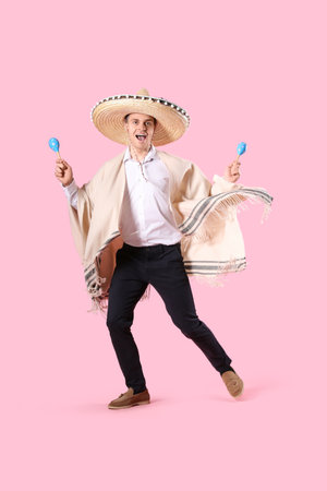 Mexican young man in sombrero hat with maracas jumping on pink backgroundの写真素材