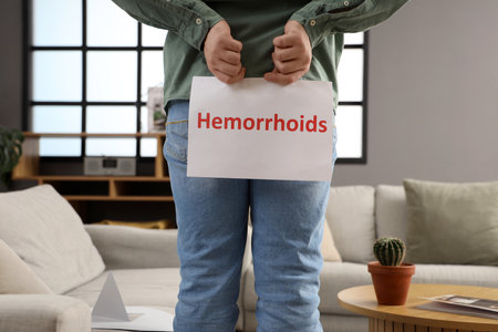 Young man holding paper with the word HEMORRHOIDS at home, back viewの写真素材